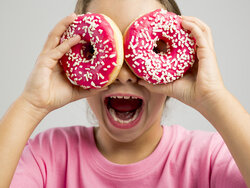 child holding pink sprinkle donuts up to eyes Austin, TX pediatric dentistry